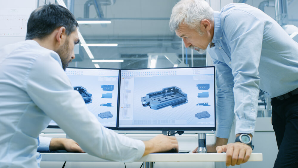 Industrial Designer Has Conversation with Senior Engineer While Working in CAD Program, Designing New Component. He Works on Personal Computer with Two Monitors. — Photo